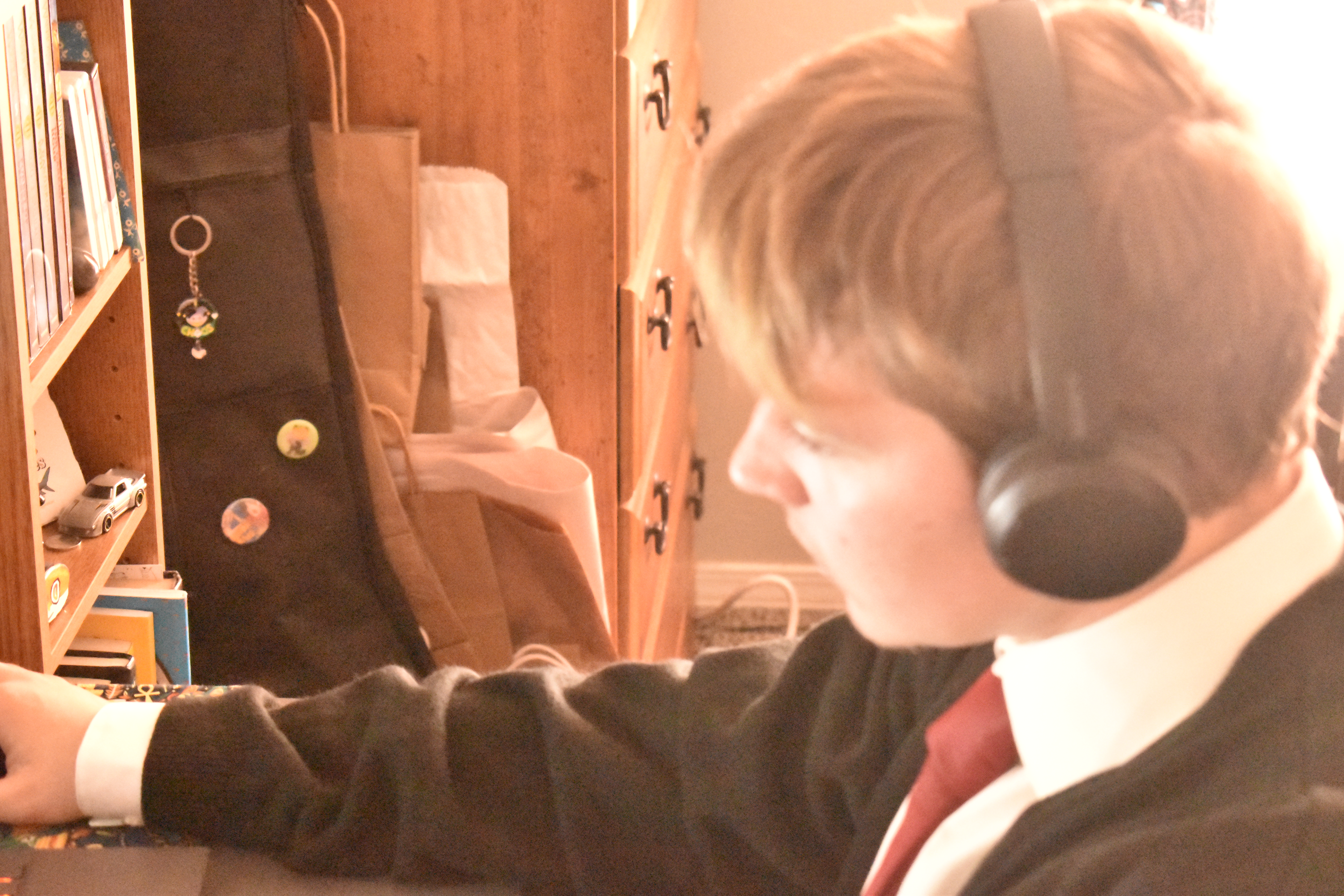 Image of me, I'm wearing a red tie with a black cardigan and white button up with my black headphones on. I'm look to the left at my computer, it's a side view.